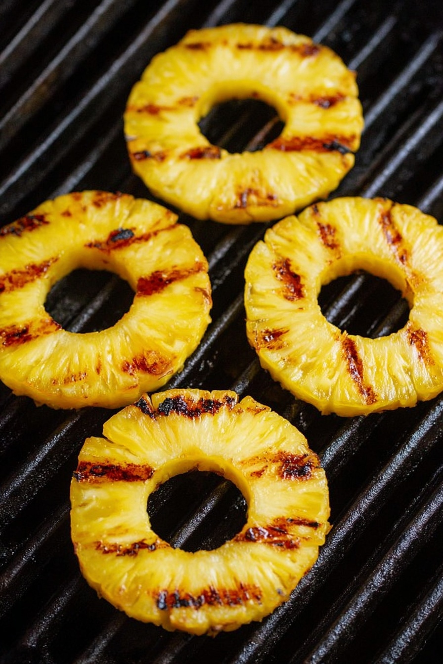 Four yellow pineapple rings with dark brown grill marks lie flat and slightly shiny on black grill bars. The pineapples have a smooth, moist texture with small charred spots and a hollow center. The grill bars run horizontally under the fruit, and the background shows depth and shadows in a close-up view. Photo taken with an iphone --ar 2:3 --v 7