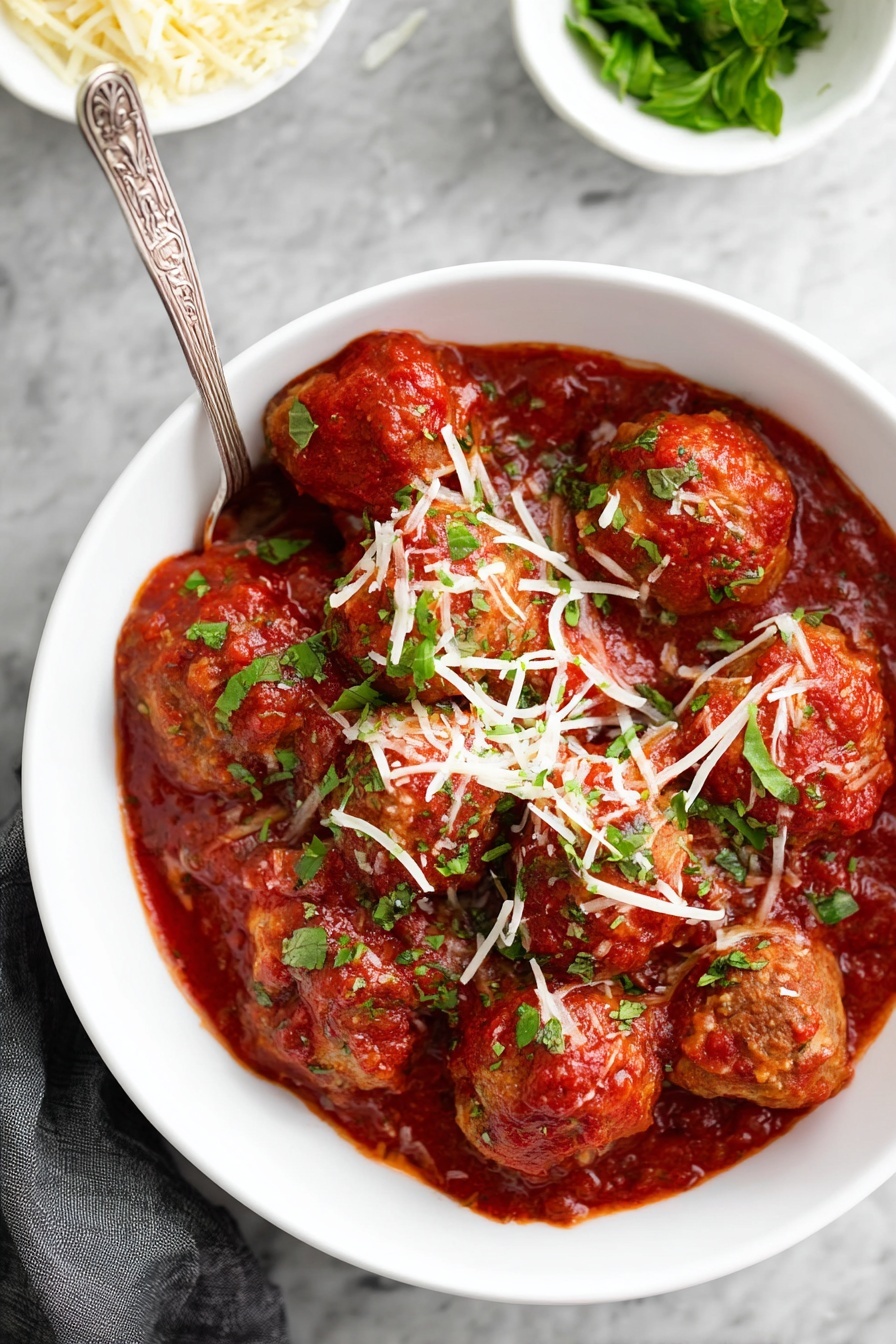 A white bowl filled with about ten round meatballs covered in thick red tomato sauce, topped with shredded light yellow cheese and chopped green herbs. The meatballs have a browned texture and are partially submerged in the sauce. A silver spoon with an ornate handle rests inside the bowl, mostly visible on the right side. The bowl sits on a white marbled surface with two small white bowls in the background, one holding green basil leaves and the other holding shredded cheese. Photo taken with an iphone --ar 2:3 --v 7