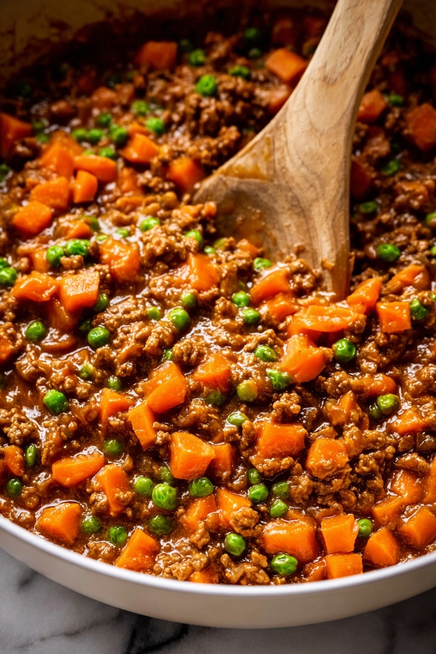 The image shows a close-up view of a cooked mixture in a large pan. The dish has three main layers: small brown minced meat pieces as the base, bright orange carrot cubes scattered throughout, and small green peas mixed evenly. The texture appears soft and moist with a shiny sauce coating all the ingredients. A wooden spoon is partially visible stirring the mixture, and the pan edges are white. The background is a white marbled surface. photo taken with an iphone --ar 2:3 --v 7