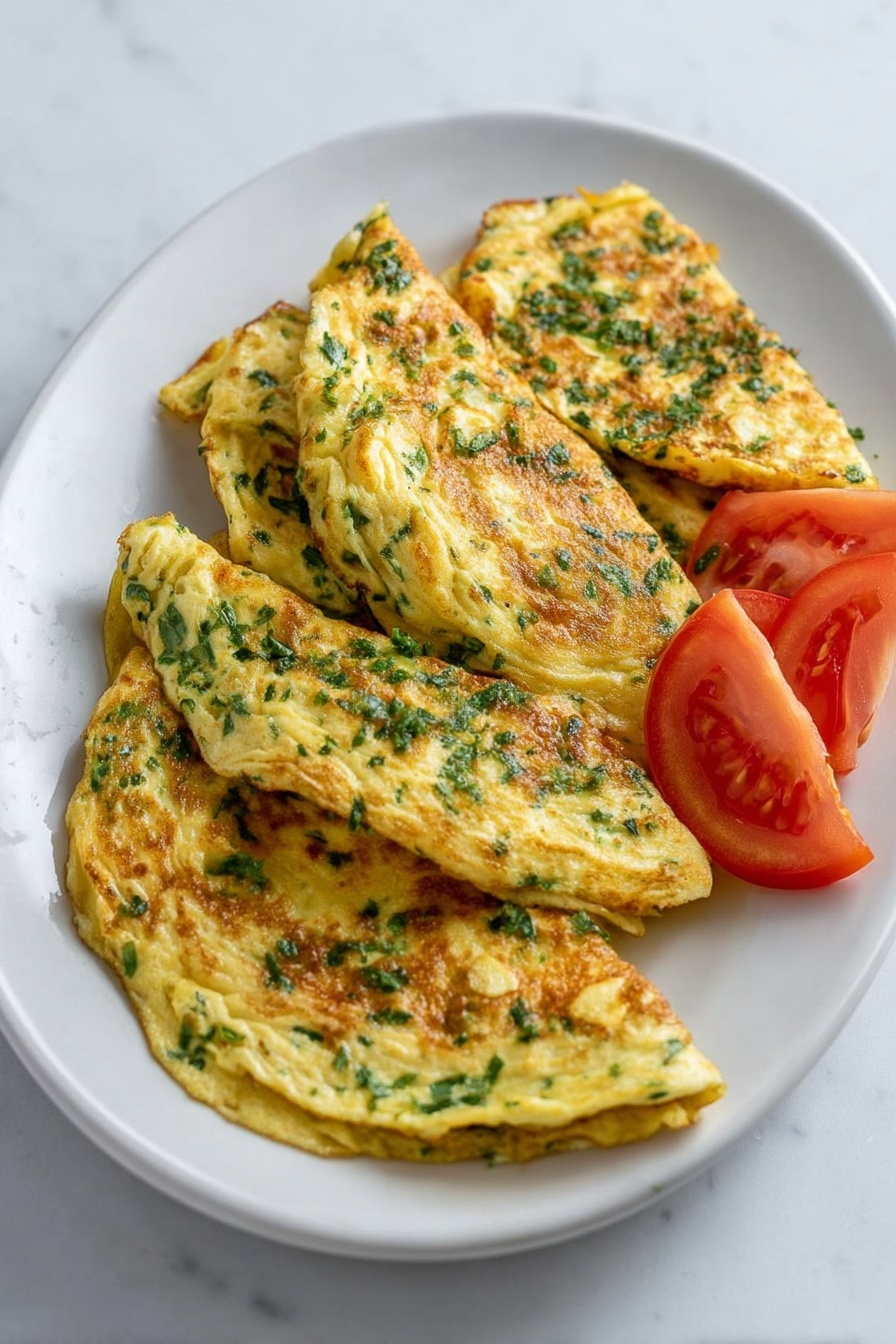 The dish shows a white oval plate with five folded omelets stacked slightly unevenly, each omelet layered with visible bits of chopped green herbs mixed in the yellow egg. The omelets have a light brown, cooked texture with some small browned spots scattered on top, highlighting a soft and tender look. Around the omelets, there are three thick wedges of fresh red tomato placed for decoration. The plate is set on a white marbled surface. photo taken with an iphone --ar 2:3 --v 7