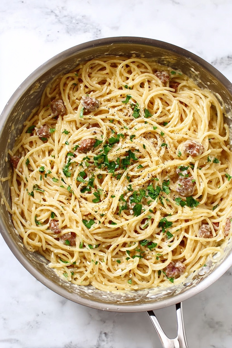 A round silver pan filled with a single layer of spaghetti noodles coated in a creamy light yellow sauce. Scattered throughout the pasta are small pieces of browned meat and bits of black pepper. The spaghetti is mixed with fresh green parsley leaves on top for color contrast. The pan is set on a white marbled surface. Photo taken with an iphone --ar 2:3 --v 7