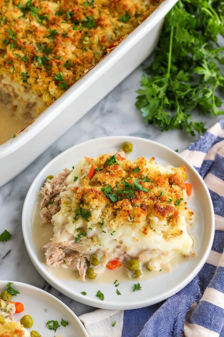 A white plate holds a layered dish with a crumbly golden brown top layer mixed with bits of green herbs and small pieces of vegetables, showing a rough texture. Underneath, creamy white sauce mixes with tender pieces of light-colored meat, creating a soft, smooth middle layer. There are green leafy garnishes placed around the edges of the plate. A gold fork held by a woman's hand is pressing into the dish, lifting some creamy and crumbly parts. The plate sits on a stack of similar white plates on a white marbled surface. Photo taken with an iphone --ar 2:3 --v 7