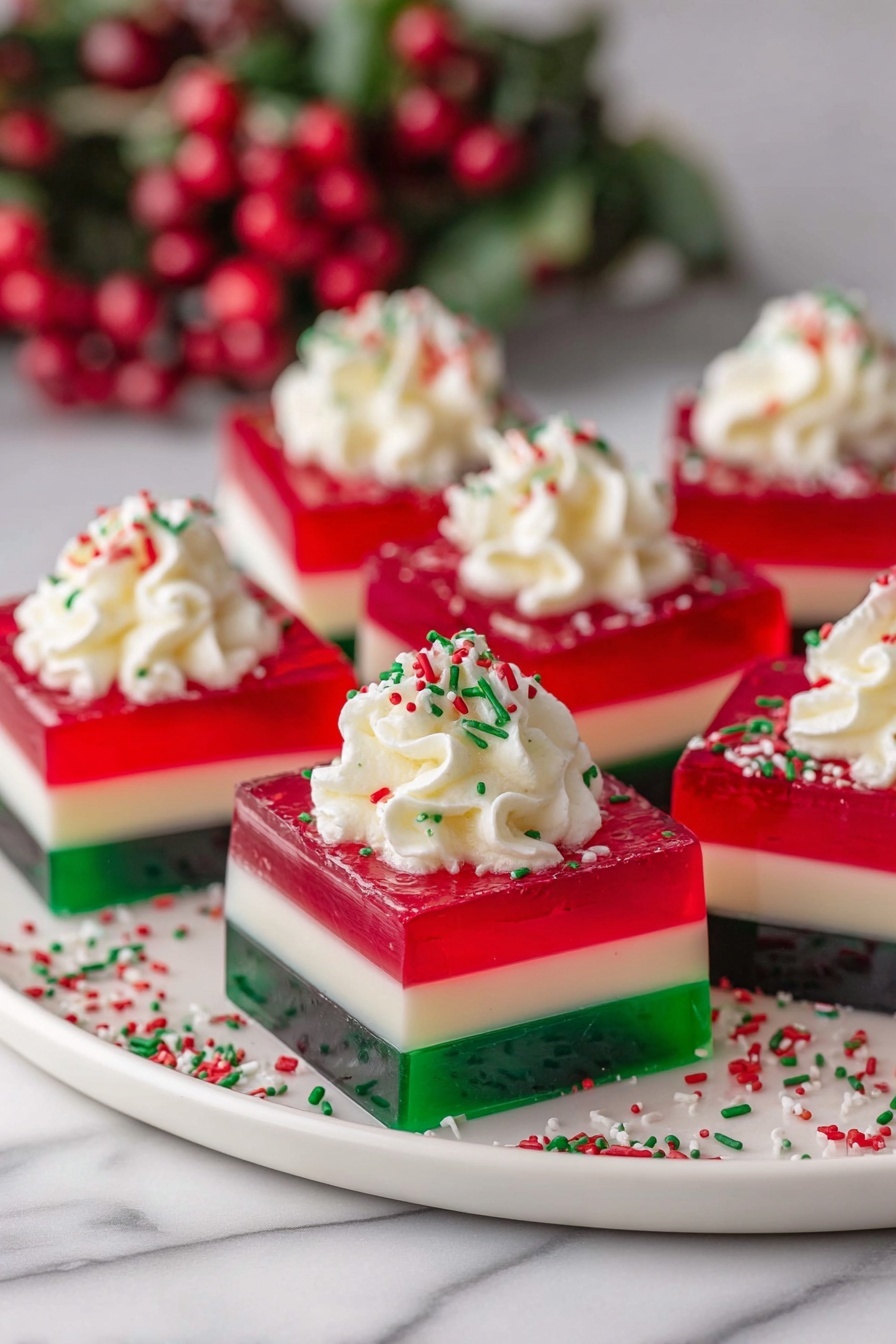 The image shows several square gelatin desserts arranged on a round white plate. Each dessert has three distinct layers: a bottom layer of dark green transparent gelatin, a middle layer of creamy white, and a top layer of bright red transparent gelatin. On top of each square is a dollop of white whipped cream, sprinkled with small red and green sprinkles. The background has a white marbled texture and there is a blurred decoration with red berries and green leaves behind the plate. Photo taken with an iphone --ar 2:3 --v 7
