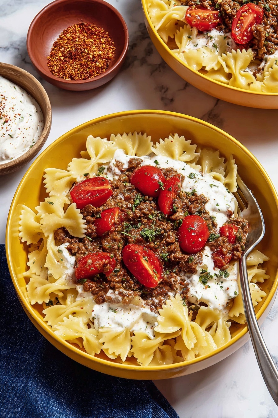 A yellow bowl holds a dish with three layers: the bottom layer is pale yellow bowtie pasta spread evenly, the middle layer is white creamy sauce dolloped thickly, and the top layer has cooked brown ground meat mixed with onions and bright red halved cherry tomatoes, sprinkled with green dried herbs. A silver fork rests inside the bowl on the right side. In the background, there is part of another identical yellow bowl with the same dish, and two small round bowls, one with red spice powder and the other with white sauce. All bowls are set on a white marbled surface with a dark blue cloth partially visible on the lower left. Photo taken with an iphone --ar 2:3 --v 7