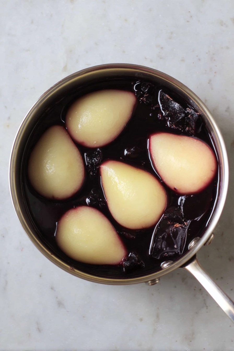 Two deep red poached pears with a shiny texture sit on top of two thin orange slices on a white plate with blue floral patterns. Next to the pears are three brown cinnamon sticks leaning to the side, and tiny pieces of green pistachios are scattered around the plate. A silver fork lies on the right edge of the plate. The background shows a white marbled texture and a blurred second plate with more orange slices, nuts, and a white bowl. Photo taken with an iphone --ar 2:3 --v 7