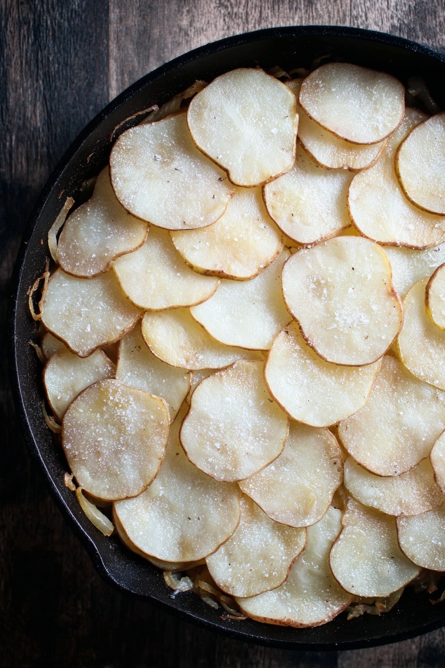 A stack of creamy potato gratin is placed in the center of a white plate with a floral pattern, showing several layers of thin, golden-brown baked potato slices covered with melted cheese and small green chopped herbs sprinkled on top. The edges show browned bits of caramelized onion mixed with the creamy sauce. A copper fork rests on the right side of the plate, and a few fresh green parsley leaves are placed for garnish around the gratin. The plate sits on a white marbled surface with a wooden texture partially visible underneath. photo taken with an iphone --ar 2:3 --v 7