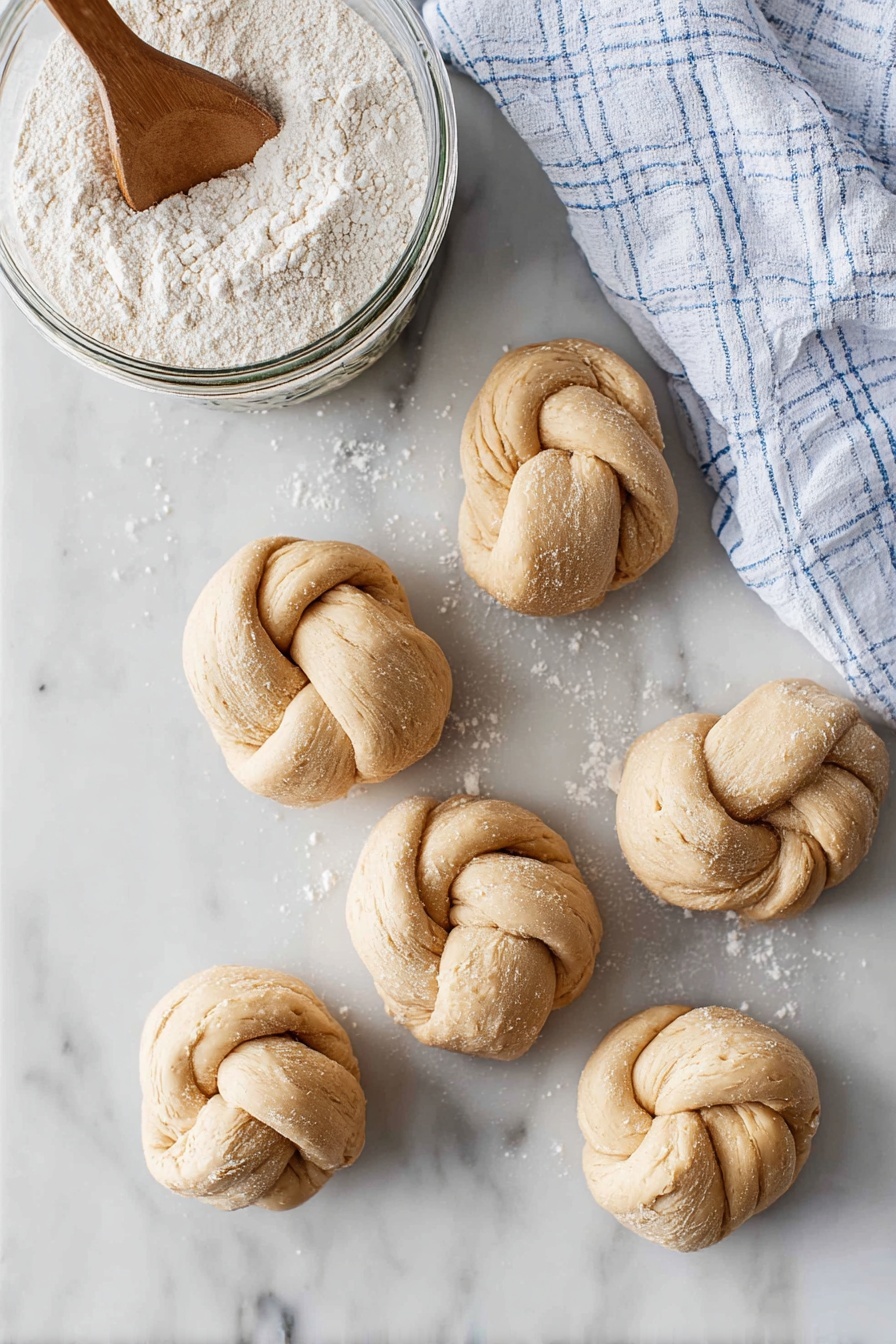 A close-up of a soft, golden bread roll made up of five small rounded sections baked together to form a flower shape. The top has a shiny, buttery glaze with some coarse salt crystals and small green herb bits sprinkled all over, adding texture and color contrast. The bread looks light and fluffy with a slight crisp on the golden-brown spots where it browned more. A woman's hand is gently holding the bread roll from the side, and the background is a white marbled texture. Photo taken with an iphone --ar 2:3 --v 7