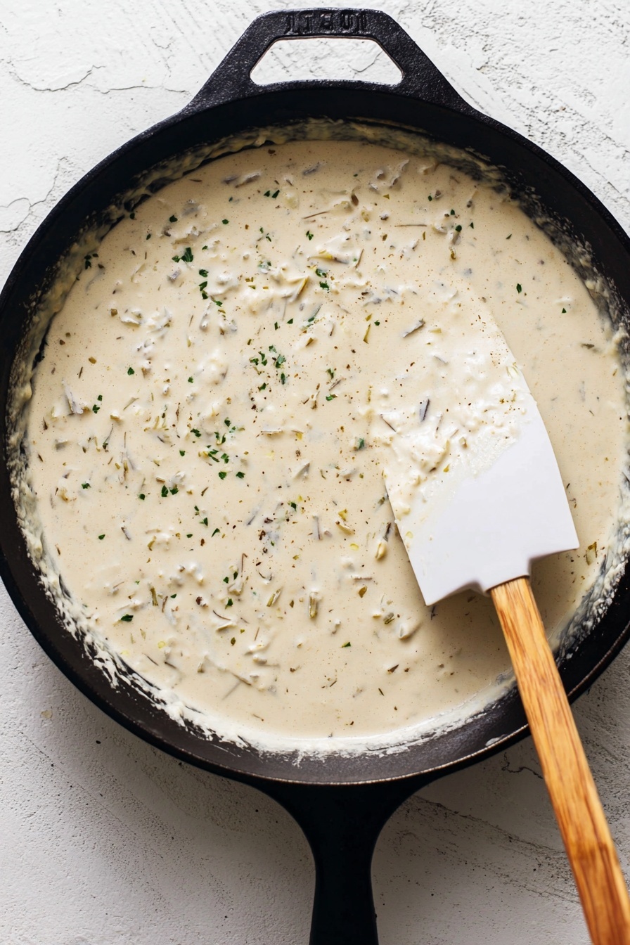 The image shows a white plate on a white marbled surface with a cheesy enchilada topped with melted yellow cheese, white sour cream sauce, chopped green herbs, and bright red tomato pieces. The enchilada is partially unrolled, revealing shredded light-colored chicken inside. Next to it is a small piece of enchilada ready to be eaten, with a silver fork resting on the plate and a silver knife beside it. Fresh green cilantro leaves decorate the plate showing a fresh look. Photo taken with an iphone --ar 2:3 --v 7